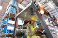 Female staff writing on clipboard while sitting on forklift in warehouse