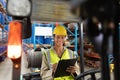 Female staff writing on clipboard while sitting on forklift in warehouse