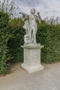 Female Statue in beautiful garden. Monument made of white stone stands on rectangular pedestal. Statue of woman which holds out Royalty Free Stock Photo