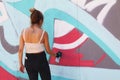 Female street artist painting colorful graffiti on wall - Modern art concept with urban girl painting live murales with aerosol co