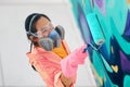 Female street artist in respirator mask painting colorful graffiti with paint roller on wall Royalty Free Stock Photo