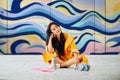 Female street artist rest sitting on the ground near the wall with her colorful paintings