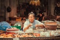 Female street vendor keeping food for sell at outdoor market with meat dishes and seafood