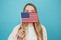 female student covering her face with a small american flag. Caucasian blonde woman holds a small american flag isolated Royalty Free Stock Photo