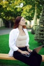 A female student in glasses sits on a bench with laptop. Freelance work in the fresh air