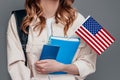 female student holding backpack, book, notebook, passport and USA flag isolated on a dark grey background