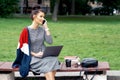 Female student with laptop is talking by cell phone while sitting on the bench Royalty Free Stock Photo