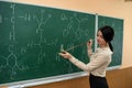 female student is practicing in a chemistry classroom with flasks on of a board with formulas. Royalty Free Stock Photo