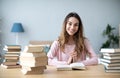 Female student sits at a table with books preparing for exams