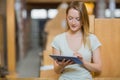 Female student sitting in library study carrel holding tablet computer and browsing digital text Royalty Free Stock Photo