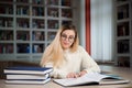 Female student taking notes from a book at library. Young woman sitting at table doing assignments in college library. Royalty Free Stock Photo