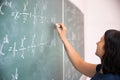 Female student or teacher in the classroom writing on chalkboard mathematical equations