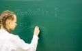 Female student teenager at a math lesson writing in chalk on a blackboard. Education, adolescence, high schoo Royalty Free Stock Photo