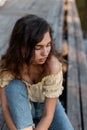 Female summer portrait of a beautiful stylish woman with curly hair in fashionable blue jeans and yellow top sits on a wooden pier Royalty Free Stock Photo