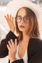 Female summer portrait of a beautiful young girl with a hat and glasses in a black blazer in the city at sunset Royalty Free Stock Photo