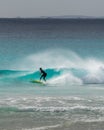 Female surfer crouches catching tube on green wave with offshore breeze causing water spray with hills in the background Royalty Free Stock Photo