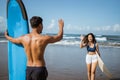 female surfer meets male friend by waving while walking with surfboard Royalty Free Stock Photo