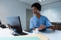 Female surgeon writing on clipboard while working on computer at desk Royalty Free Stock Photo