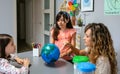 Female teacher giving ecology lesson with handmade globe world to girl students