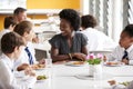 Female Teacher With Group Of High School Students Wearing Uniform Sitting Around Table And Eating Lunch In Cafeteria Royalty Free Stock Photo