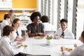 Female Teacher With Group Of High School Students Wearing Uniform Sitting Around Table And Eating Lunch In Cafeteria Royalty Free Stock Photo