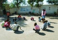 Female teacher in head scarf at school collecting the girls in circle and drawing on the sand