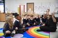 Female teacher holding up a book in front of her class of elementary school kids sitting on the floor in a classroom, side view Royalty Free Stock Photo