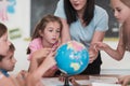 Female teacher with kids in geography class looking at globe. Side view of group of diverse happy school kids with globe Royalty Free Stock Photo