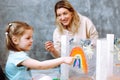 Female teacher with little blonde girl painting rainbow on oilcloth. Fun learning in kid development childcare center Royalty Free Stock Photo