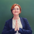 Female teacher stands with a beatific face and hands clasped in prayer. Holy schoolteacher with red hair Royalty Free Stock Photo