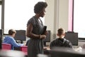 Female Teacher Supervising Line Of High School Students Working at Screens In Computer Class