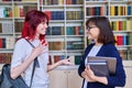 Female teacher talking to teenage student girl, inside library Royalty Free Stock Photo