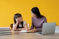 A female teacher is teaching math to a cute little girl at a study table. isolated yellow background Royalty Free Stock Photo