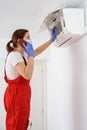 Female technician using smartphone and repairing air conditioner Royalty Free Stock Photo