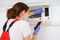 Female technician using smartphone and repairing air conditioner Royalty Free Stock Photo