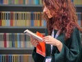 Female teenager red haired choosing a book in colorful bookstore