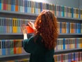 Female teenager red haired choosing a book in colorful bookstore