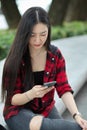 Female teenager sitting in city street, messaging to her friends, using smartphone