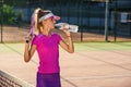 Female tennis player in pink uniform drinking water from plastic bottle after tennis training on the outdoor court at Royalty Free Stock Photo