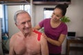 Female therapist applying elastic therapeutic tape on shoulder of smiling shirtless senior male pati Royalty Free Stock Photo