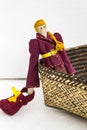 A female tilde doll in colorful clothes is sitting in a wicker basket on a white background. Registration of holidays