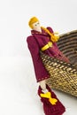 A female tilde doll in colorful clothes is sitting in a wicker basket on a white background. Registration of holidays