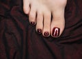 Female toes with beautiful bloody red glossy pedicure on the drape of dark shiny fabric, close up. Bare foot. Royalty Free Stock Photo