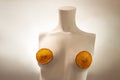 Female torso from a mannequin. Conceptual art. A minimalist female bust with orange slices on the nipples. Product advertisement