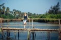 A female tourist in denim shorts with short haircut on sunny tropical day. Young pretty girl stands on wooden bridge over small Royalty Free Stock Photo