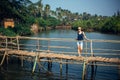 A female tourist in denim shorts with short haircut on sunny tropical day. Young pretty girl stands on wooden bridge over small Royalty Free Stock Photo