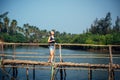 A female tourist in denim shorts with short haircut on sunny tropical day. Young pretty girl stands on wooden bridge over small Royalty Free Stock Photo