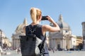 Female tourist with a fashinable vintage hipster backpack taking photo oof Piazza del Popolo in Rome, Italy by her Royalty Free Stock Photo