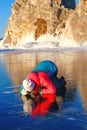 Female tourist looks through a transparent ice. Pure Baikal ice. Warm clothing. Winter vacation