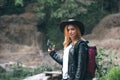 Female tourist use smartphone, with backpack and cowboy hat looking at the river washed away the bridge, the crossing was